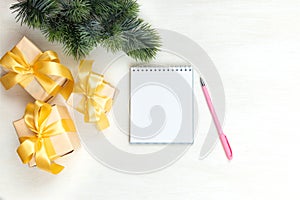 Christmas festive composition. White notepad, pink pen, gifts with a gold bow on a light table. Flat lay, top view