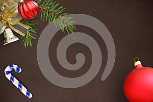 Christmas fir branch, red wavy dull ball, stick and bell on dark background