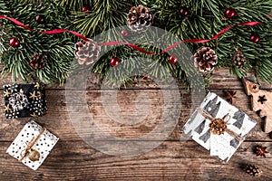 Christmas fir branches on holiday wooden background with gift boxes, pine cones, red decoration.