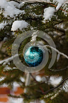 Christmas fir tree branch covered with snow and decorated with virid, emerald bauble outdoors, vertical shot