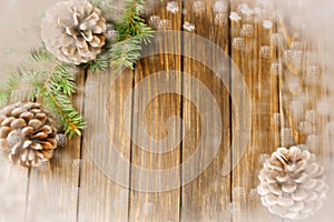 Christmas fir tree and cones on brown wooden background with snowflakes