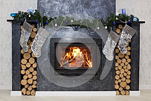 Christmas fireplace with a fire burning in it, new year garland and firewood for kindling. A silver-gray fireplace