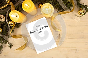 Christmas flat lay for a book presentation: book with blank cover settled with three lit candles , white organza and gold satin