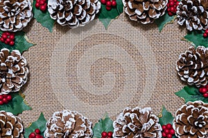 Christmas flat-lay frame of pinecones, holly leaves, and red berries on rustic fabric background