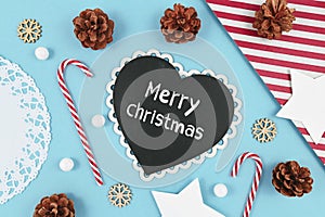 Christmas flat lay with heart shaped chalkboard with text `Merry Christmas` on light blue background with seasonal decoration