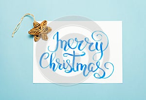 Christmas flat lay: lettering text `Merry Christmas` and vintage wooden star on blue background.