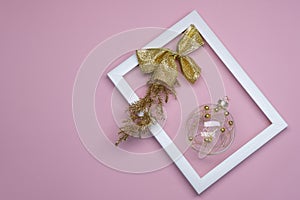 Christmas flat lay on pink background. In white frame ball with gold bow and coniferous twig.