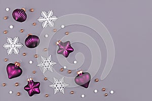 Christmas flat lay with purple heart and star shaped and round tree ornament baubles and white snowflakes on gray background