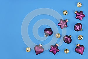 Christmas flat lay with purple tree ornament baubles and golden bells in corner of blue background with copy space