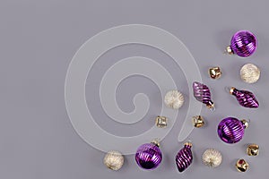 Christmas flat lay with purple and white tree ornament baubles and golden bells in corner of gray background with copy space