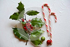 Christmas flat lay scene with two candy canes, green and red holly with ornaments