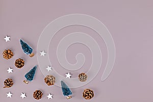 Christmas flat lay with small Christmas trees, pine cones and wooden star ornaments in corner of gray background