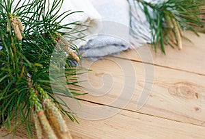 Christmas flatlay on a rustic wooden background: green pine needles with cones, warm woolen things in white and blue. New year`s c