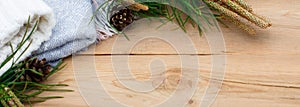 Christmas flatlay on a rustic wooden background: green pine needles with cones, warm woolen things in white and blue. New year`s c