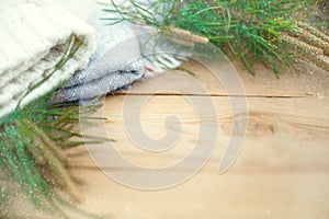 Christmas flatlay on a rustic wooden background: green pine needles with cones, warm woolen things in white and blue. New year`s