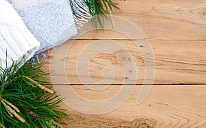Christmas flatlay on a rustic wooden background: green pine needles with cones, warm woolen things in white and blue. New year`s c