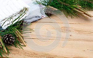 Christmas flatlay on a rustic wooden background: green pine needles with cones, warm woolen things in white and blue. New year`s c