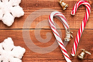 Christmas flatlay: white soft decorative snowflakes and two candies cane with three golden bells on wooden background