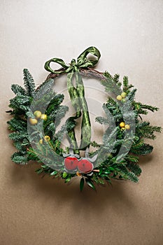 Christmas floral wreath decoration with baubles, red bow, holly and winter greenery over kraft background.