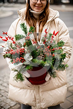 Christmas flower arrangement in pot of spruce branches and red berries and eucalyptus in female hands