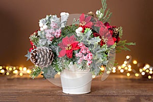 Christmas flower bouquet with red poinsettia, pine cones and spruce branches, festive arrangement on brown background with bokeh