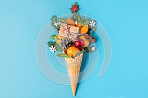 Christmas food concept. tangerine fruits, gift box and Christmas decorations in waffle ice cream cone on blue background