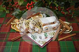 Christmas food photography image with stollen cake bread cinnamon sticks cut holly leaves and berries on green red kitchen table