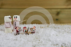 Christmas food photography using marshmallows shaped as snowman with iced on smile and standing in snow with Santa Claus ornaments