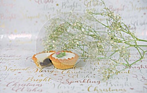 Christmas food photography of white green flowers with glitter and mince pies on xmas wrapping paper background