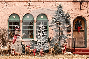 Christmas forest tableau with snowman and be-ribboned deer outside windows of pink stucco house