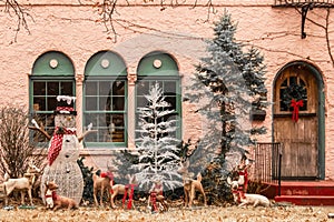 Christmas forest tableau with snowman and be-ribboned deer outside windows of pink stucco house photo