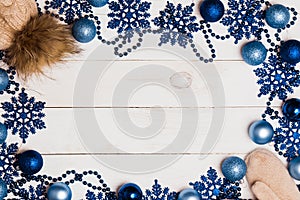 Christmas frame of blue balls, beads, stars and warm knitted hats and mittens on a white wooden table, top view, copy space.