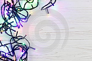 christmas frame of garland lights. colorful stylish border on white rustic wooden background. space for text. holiday greeting ca