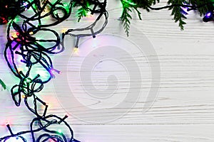 christmas frame of garland lights on fir branches. stylish border on white rustic wooden background. space for text. holiday