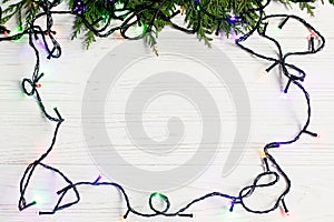 christmas frame of garland lights on fir branches. stylish border on white rustic wooden background. space for text. holiday