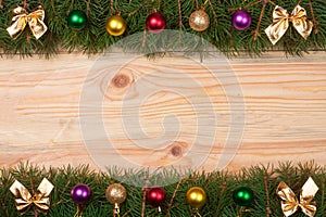 Christmas frame made of fir branches decorated with golden bows and balls on a light wooden background