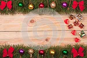Christmas frame made of fir branches decorated with red bows and balls on a light wooden background