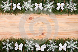 Christmas frame made of fir branches decorated with snowflakes and white bows on a light wooden background