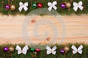 Christmas frame made of fir branches decorated with white bows and balls on a light wooden background