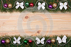 Christmas frame made of fir branches decorated with white bows beads and balls on a light wooden background