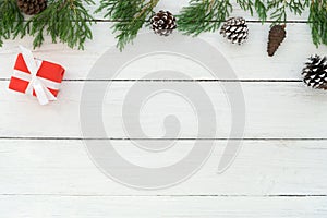 Christmas frame made of fir leaves, pine cones and red gift box with decoration rustic elements on white wooden.