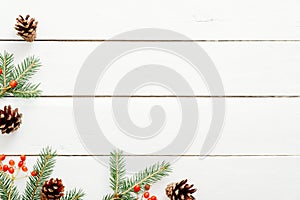 Christmas frame made of fir tree branches, red berries, pine cones on rustic wooden white desk. Christmas, New Year, winter