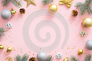 Christmas frame made of golden and silver balls, fir tree branches, star, gift boxes, pine cones on pastel pink background. Flat