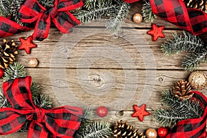 Christmas frame of ornaments, branches and buffalo plaid check ribbon on a rustic wood background