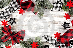 Christmas frame of ornaments, branches and buffalo plaid ribbon on a rustic white wood background