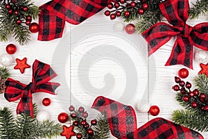 Christmas frame of ornaments, branches and red and black checked buffalo plaid ribbon, top view on a white wood background