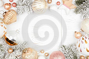 Christmas frame of snowy branches and dusty rose, gold, and white ornaments on a white wood background