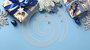 Christmas frame top border made of fir tree branches, gift boxes, silver blue stars, balls over blue background. Flat lay, top