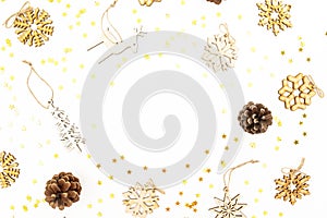 Christmas frame with wooden tree decoration, snowflakes, golden confetti and pine cones on white background. Flat lay, top view. N