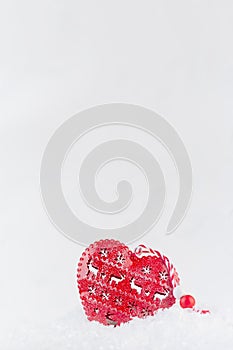Christmas fun decoration - cute red heart with festive ornament in white sparkling fluffy snow, copy space, vertical.